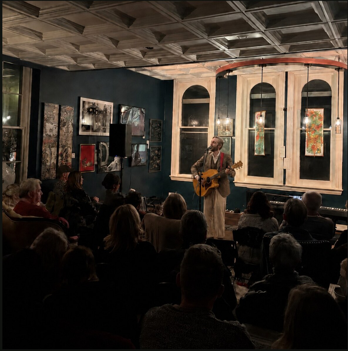 Robert Rosina performing acoustic guitar for an audience in an intimate room